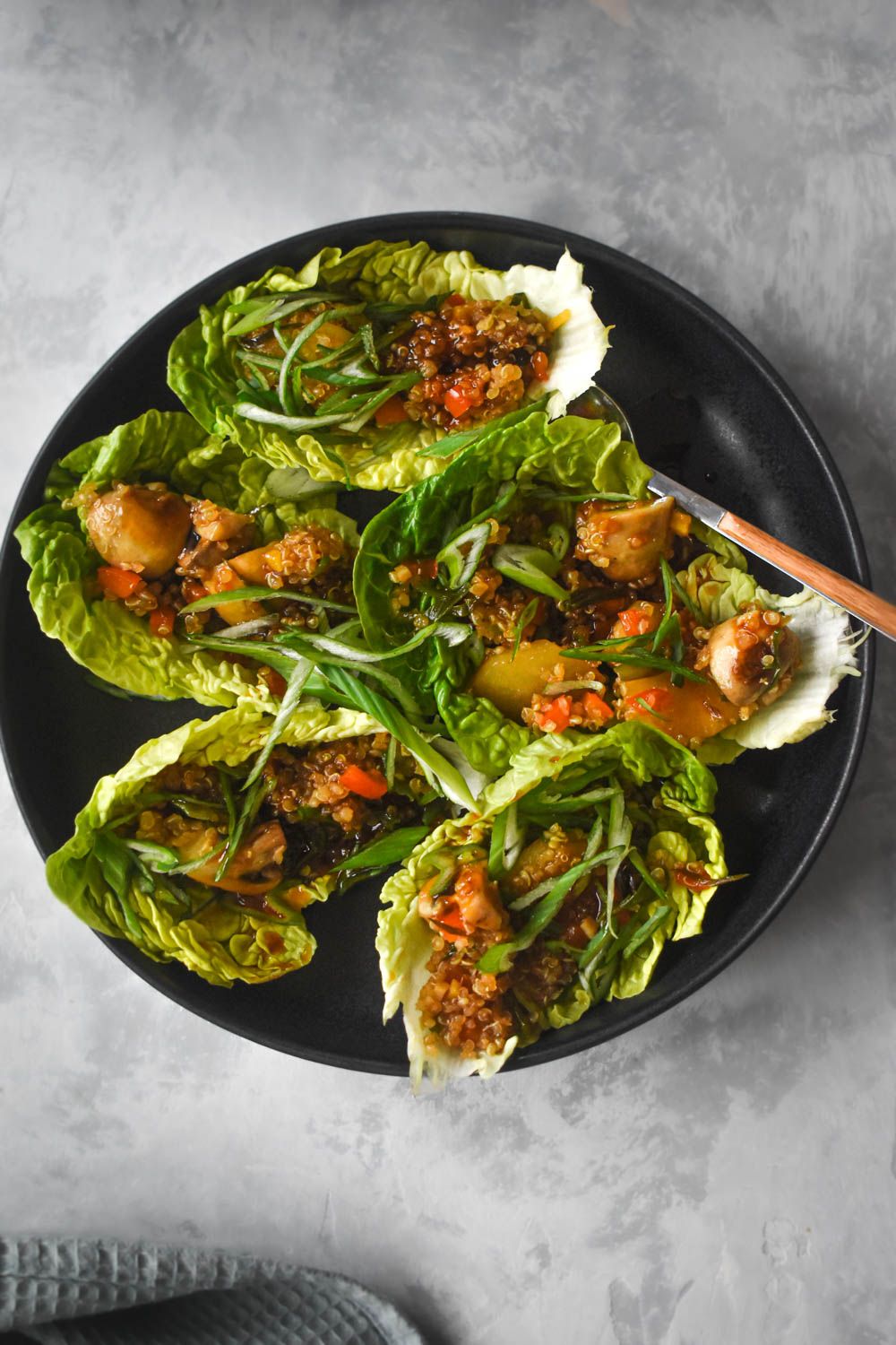 Asian vegetarian lettuce wraps with quinoa, mushrooms, red peppers, and water chestnuts in lettuce leaves on a plate.