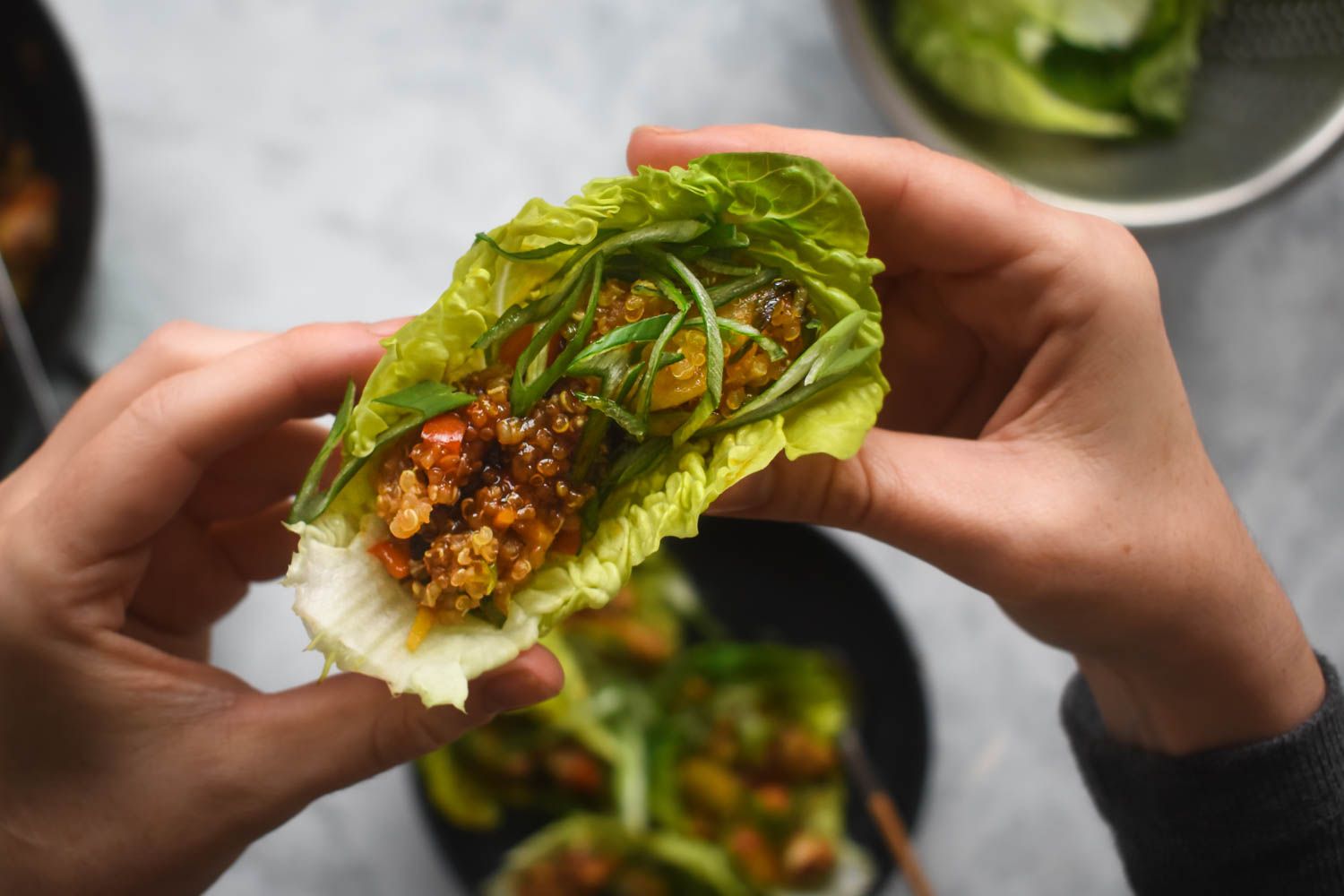 Lettuce wraps with vegetarian quinoa filling being picked up by a hand.