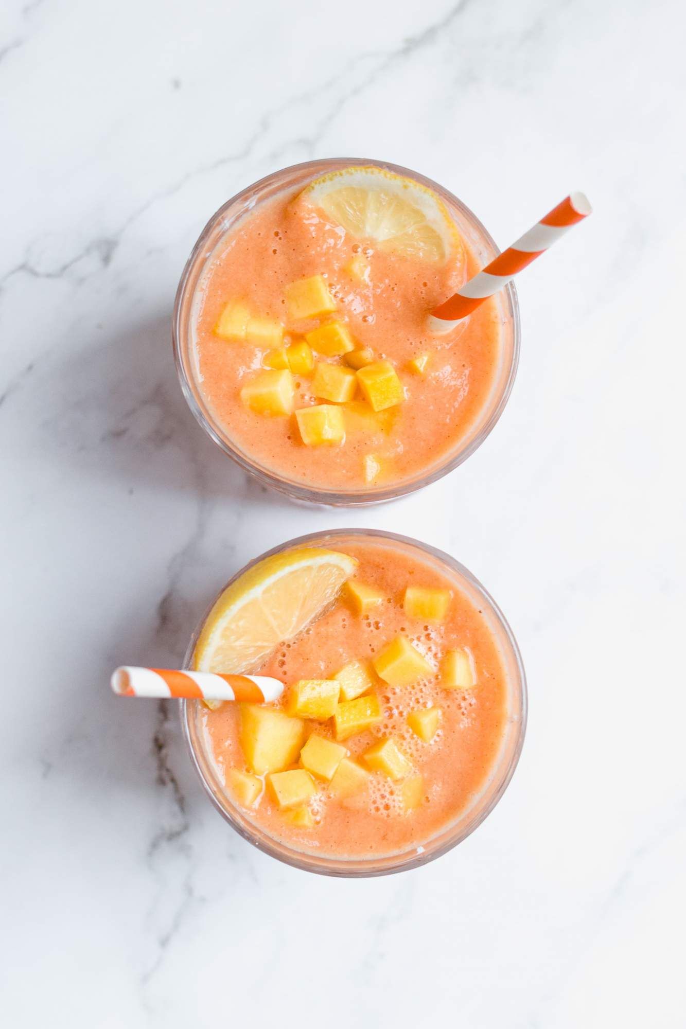 Carrot smoothies with frozen mango and lemon juice poured into two glasses.