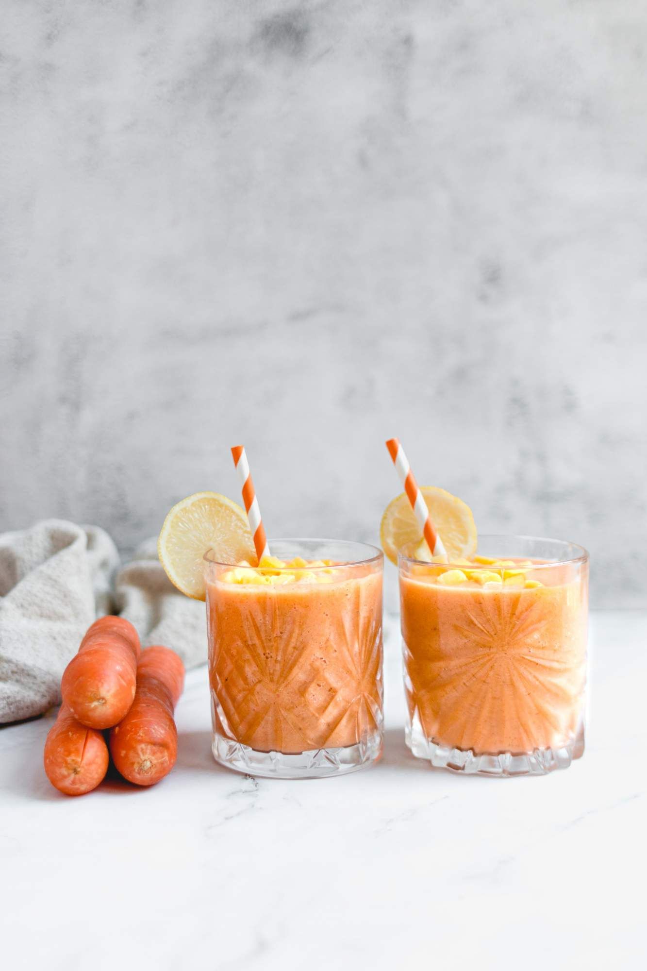 Creamy carrot and ginger smoothie with mangos, bananas, carrots, ginger, and almond milk  poured in two glasses.