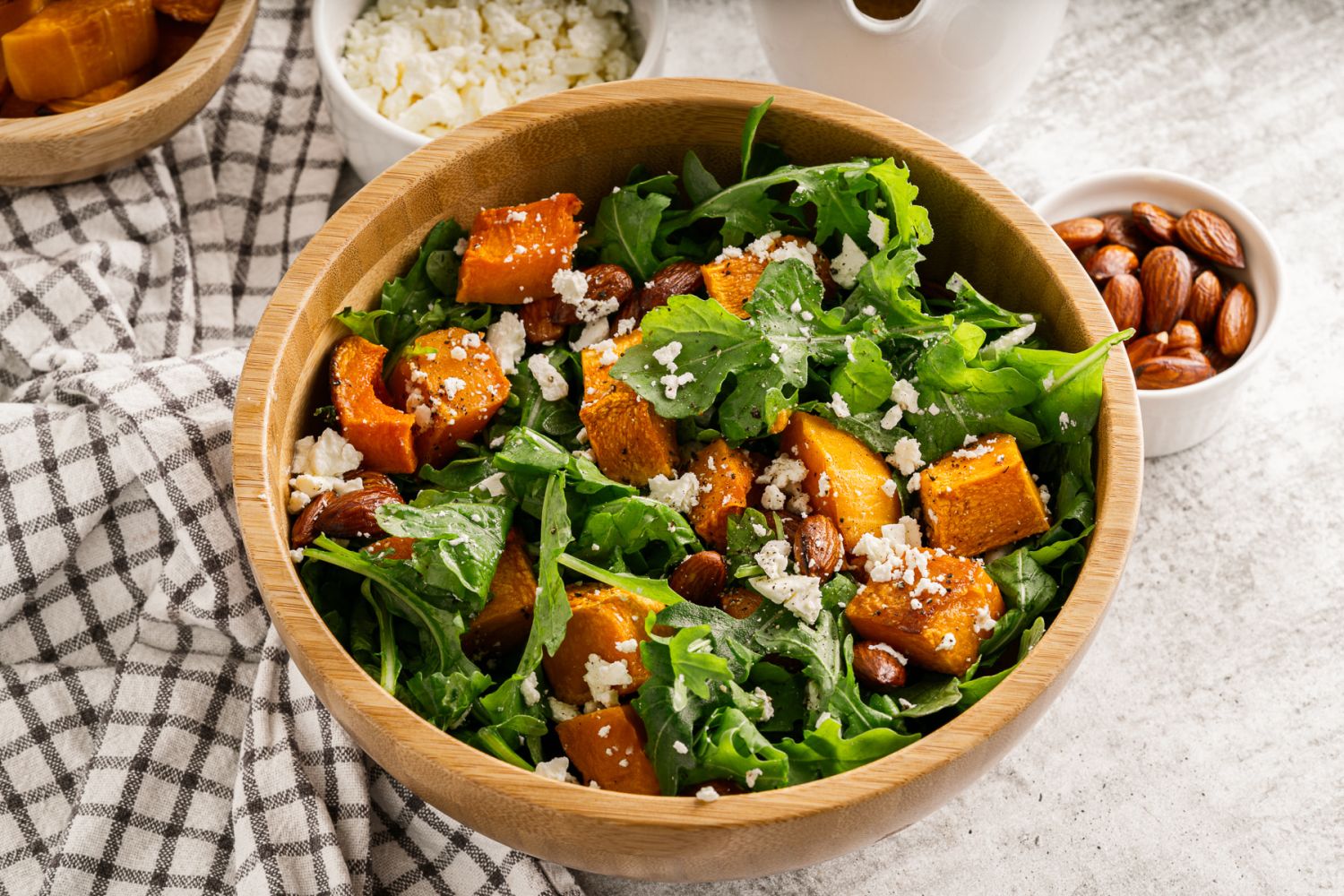 Arugula butternut squash with feta cheese and almonds in a wooden bowl with almonds on the side.