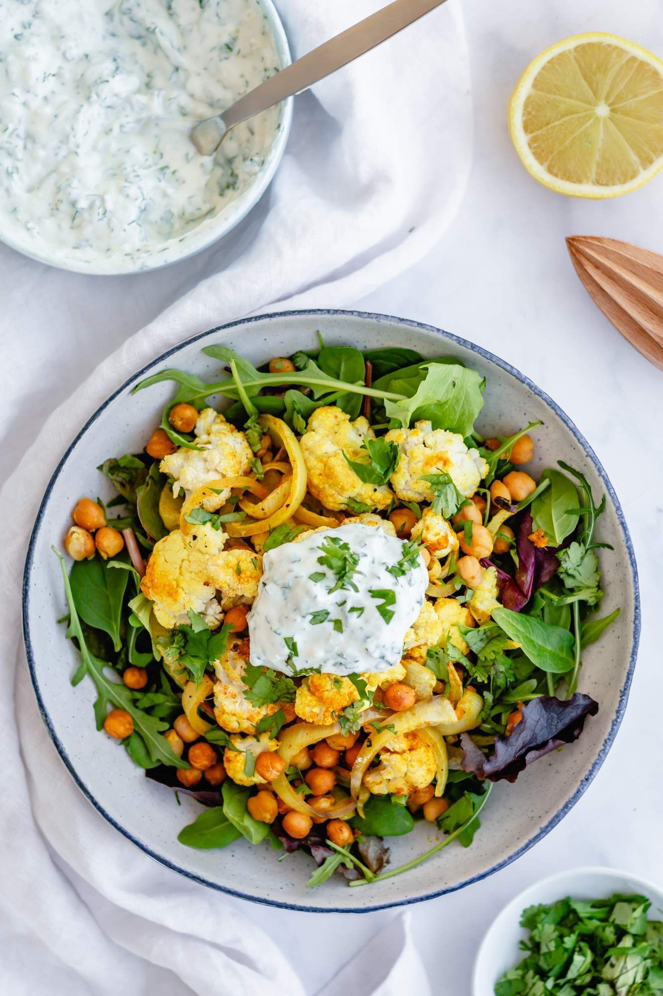 Chickpeas with cauliflower and yogurt sauce in a bowl with mixed greens and roasted onions.