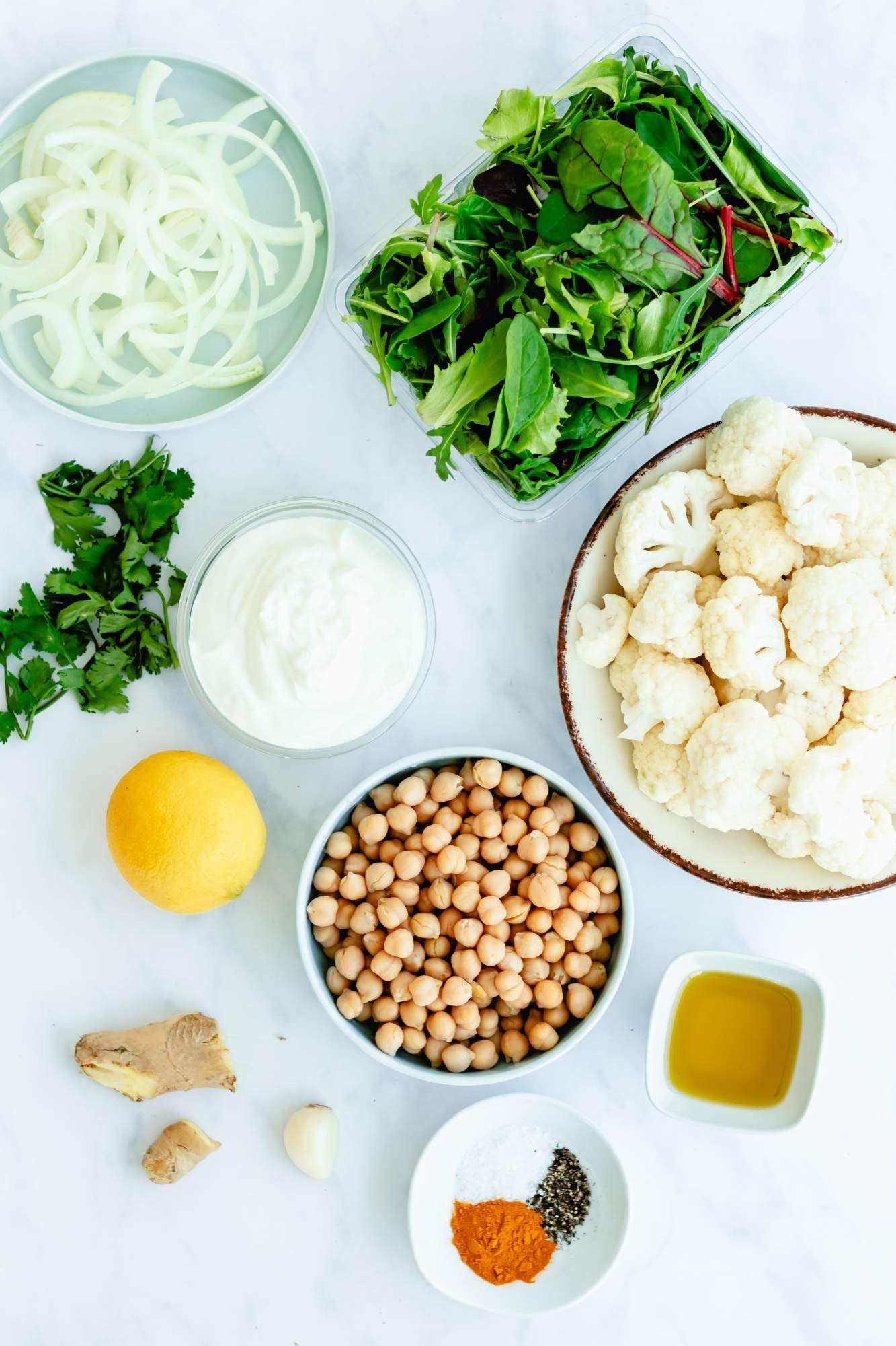 Ingredients to make roasted cauliflower and chickpeas including onions, curry powder, cilantro, chickpeas, and cauliflower.