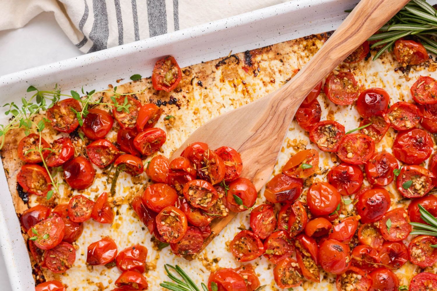 Garlic roasted cherry tomatoes with fresh herbs being scooped with a wooden spoon.