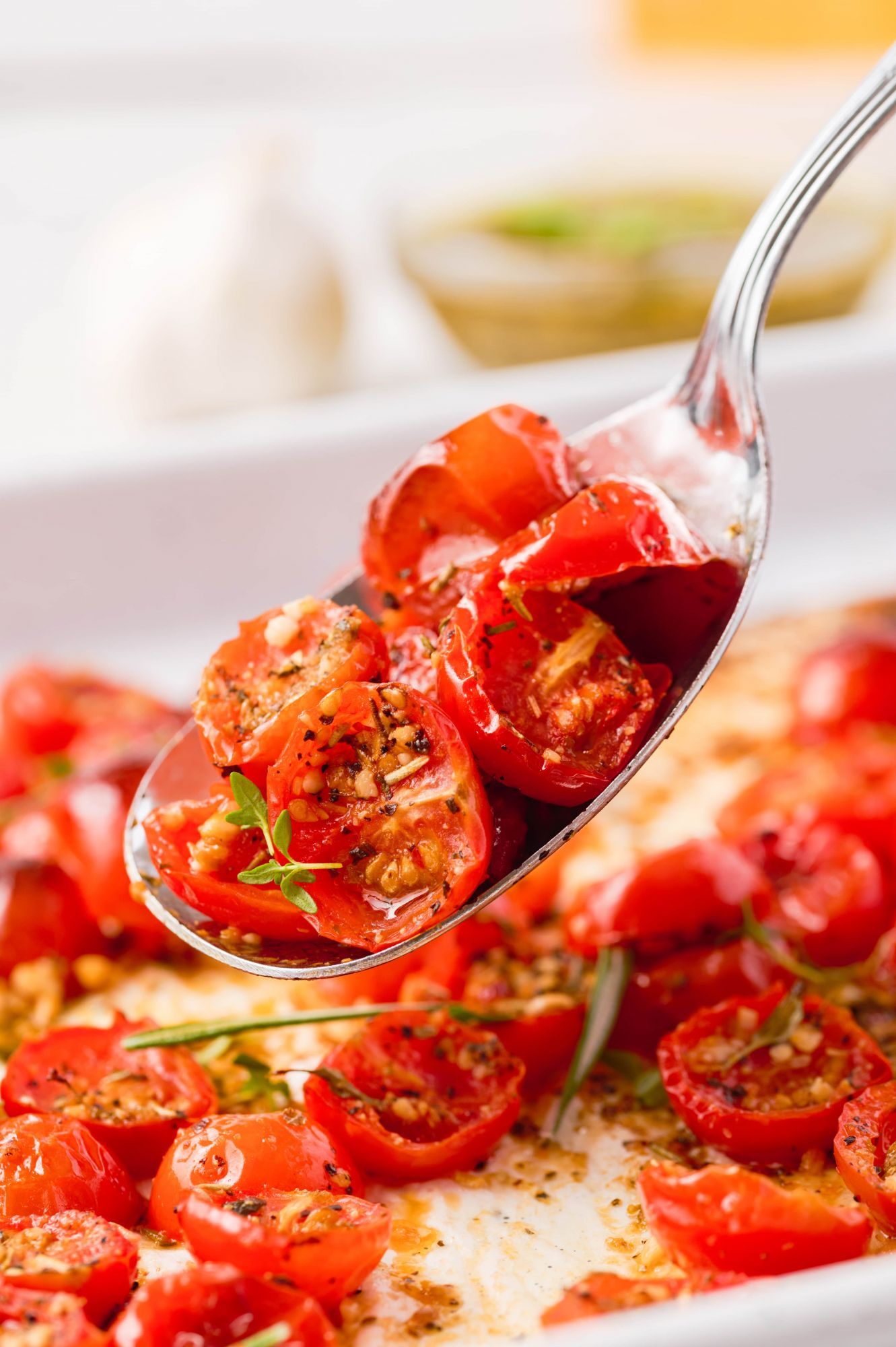 Oven roasted cherry tomatoes with minced garlic, Italian seasoning, and olive oil on a silver spoon.