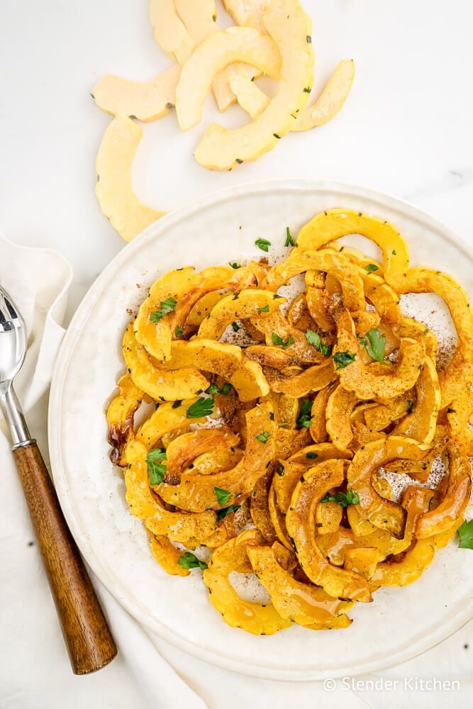 Cooked Delicata squash on a white plate with raw squash on the side.