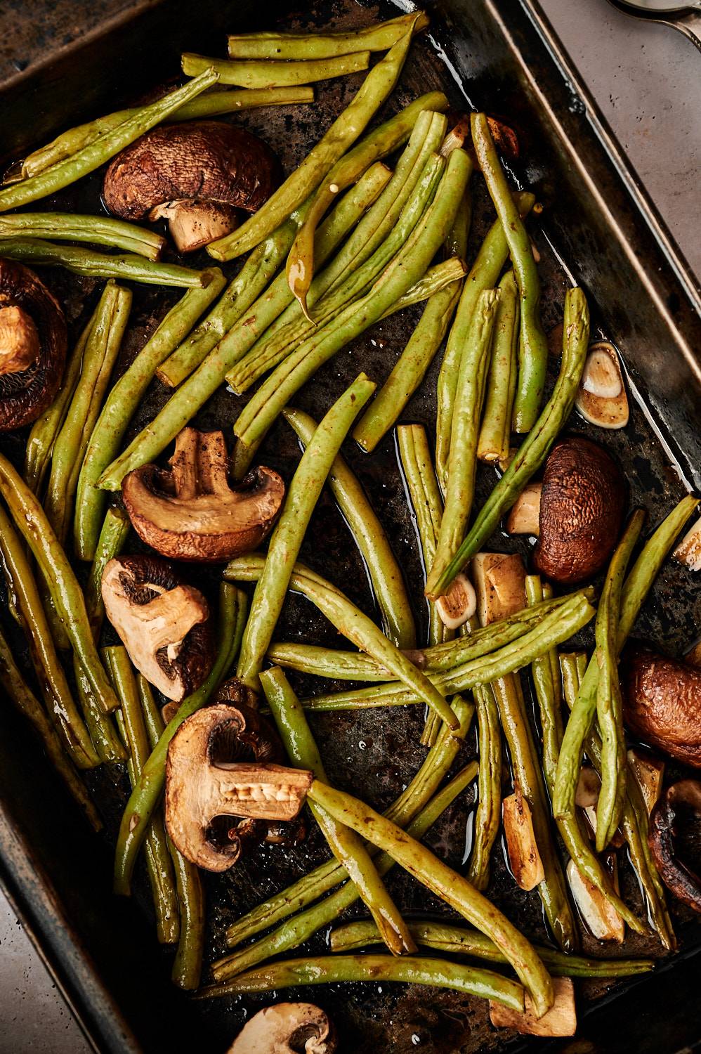 Balsamic green beans and mushrooms on a baking sheet with garlic slices.