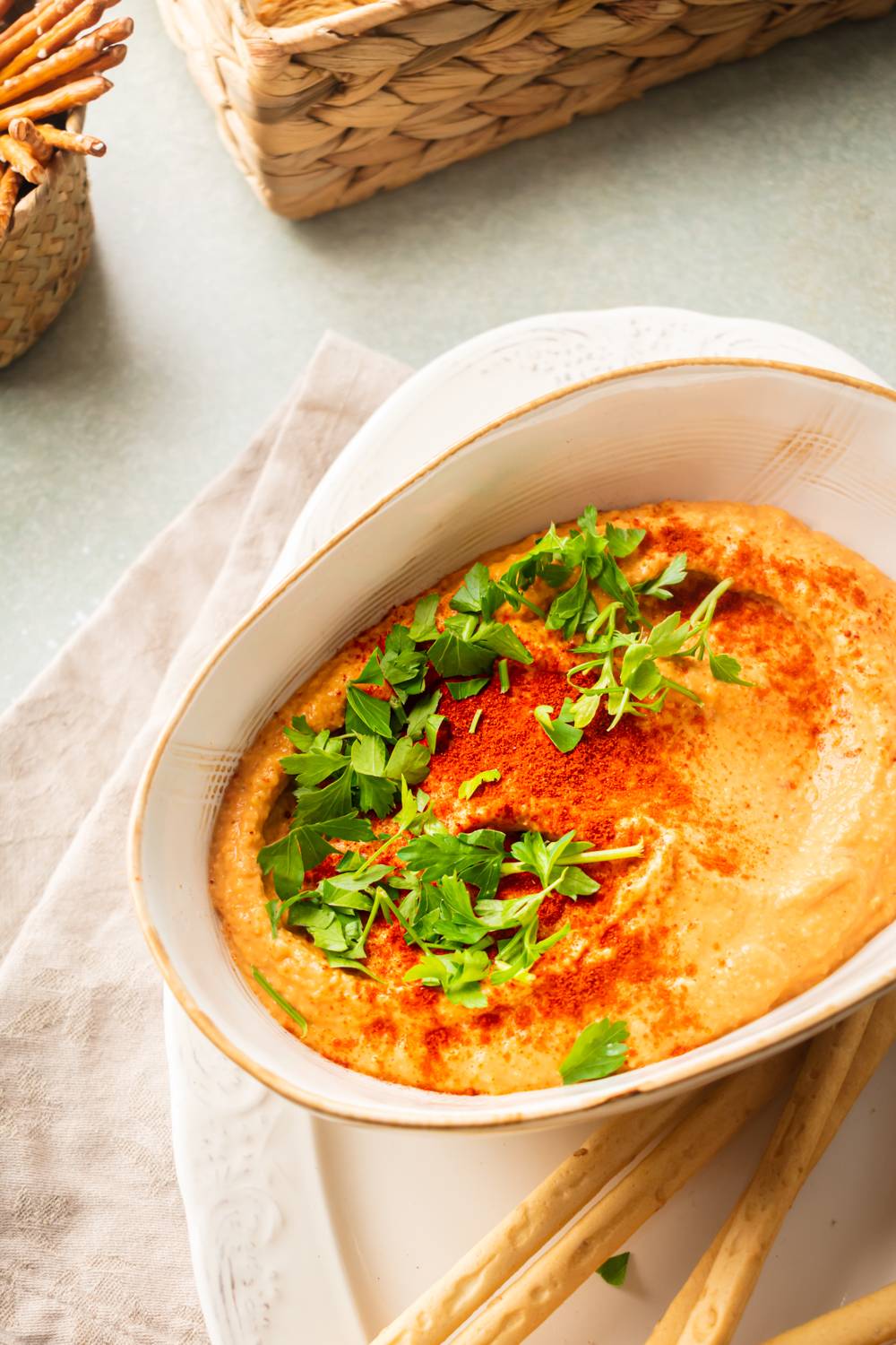 Hummus with roasted red peppers served in a bowl with breadsticks on the side.