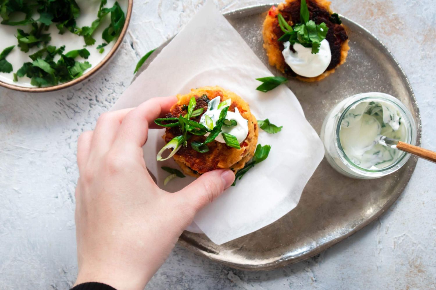 Salmon cakes with crispy golden brown edges stacked on a plate with yogurt and green onions.