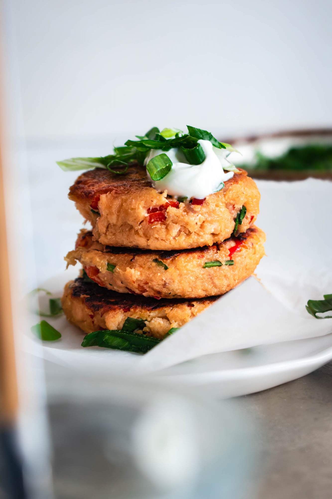 Homemade salmon patties with canned salmon with spices stacked on a plate with green onions and yogurt.