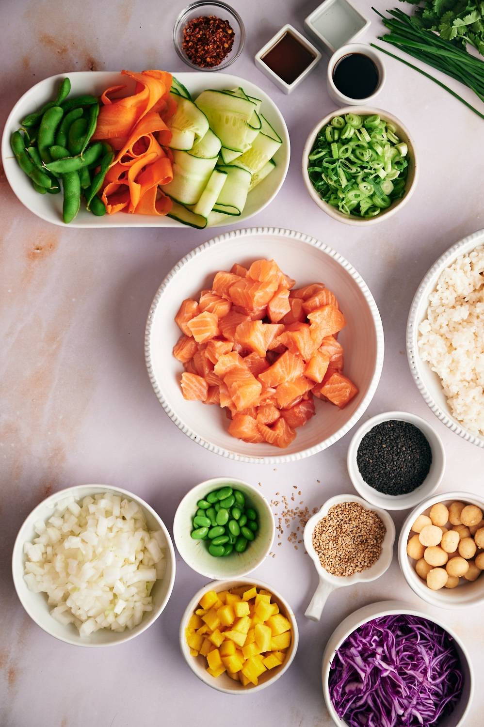 Ingredients for salmon poke bowls including raw salmon, rice, soy sauce, edamame, green onions, carrots, cucumbers, and more.