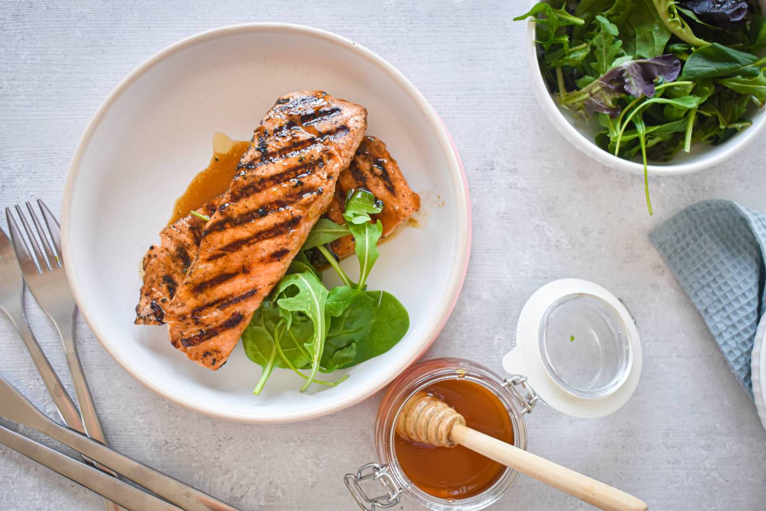 Grilled salmon recipe on a plate with honey and lime sauce with salad on the side.