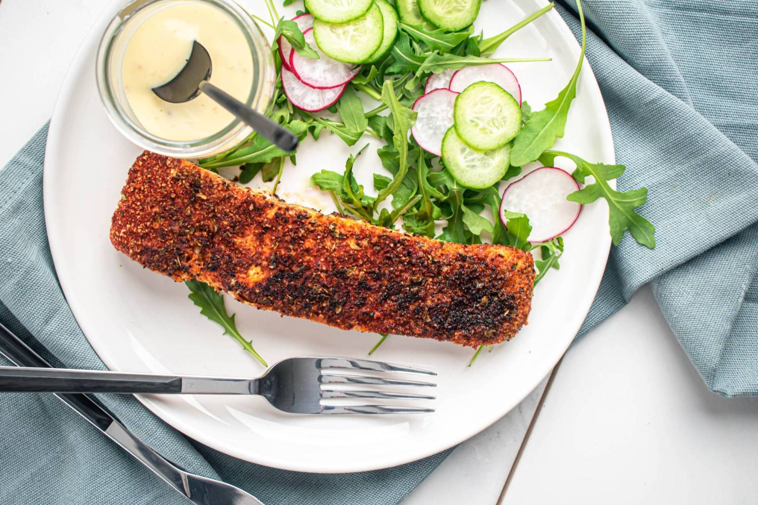 Blackened salmon with a homemade seasoning blend on a plate with salad and mustard sauce.