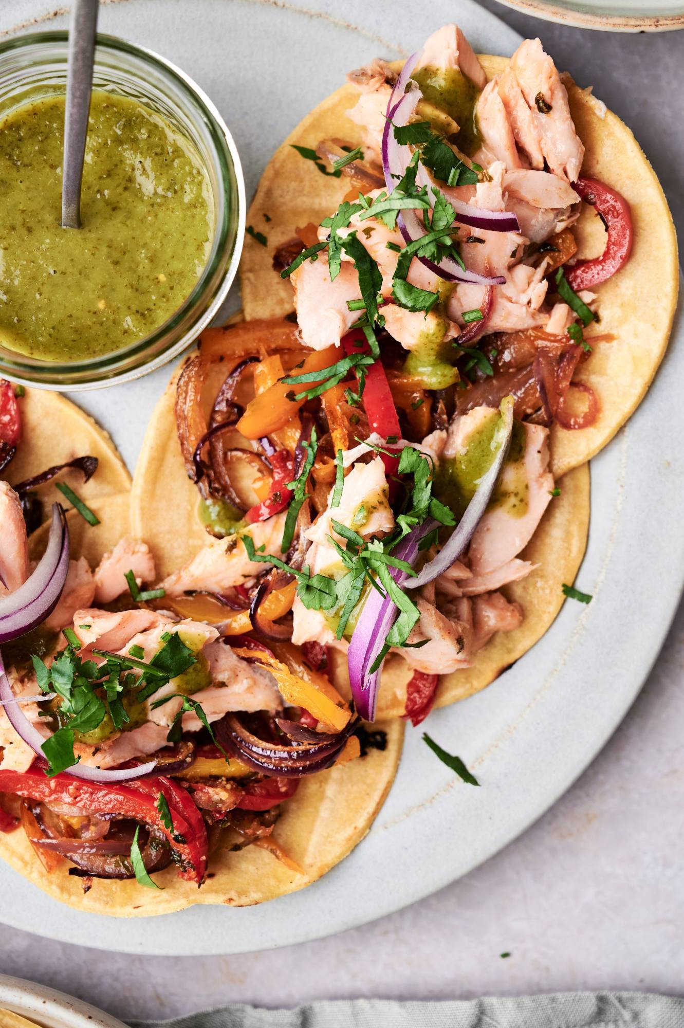 Easy salmon fajitas on a plate with peppers, onions, cilantro, limes, and green salsa.