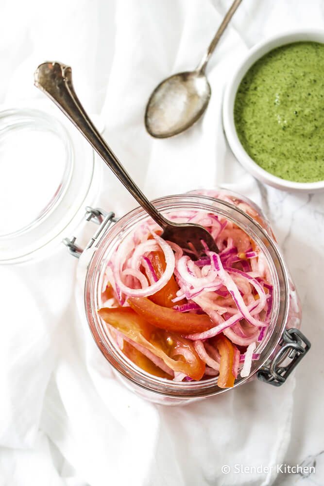 Salsa criolla with pickled red onions, chopped tomatoes, lime juice, peppers, and cilantro in a glass jar.
