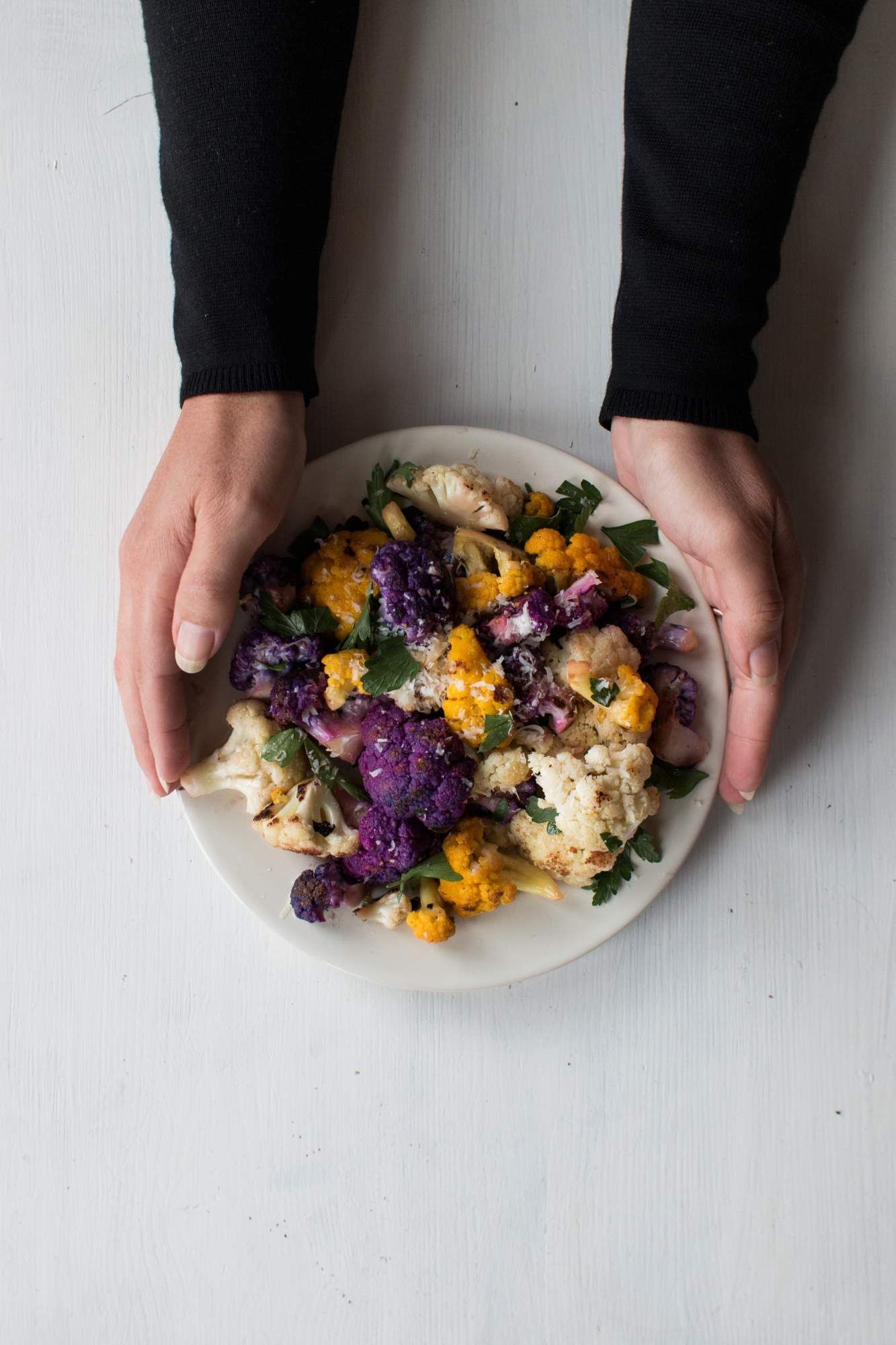 Cauliflower that is sauteed with garlic and olive oil on a plate with fresh parsley, lemon, and Parmesan cheese.