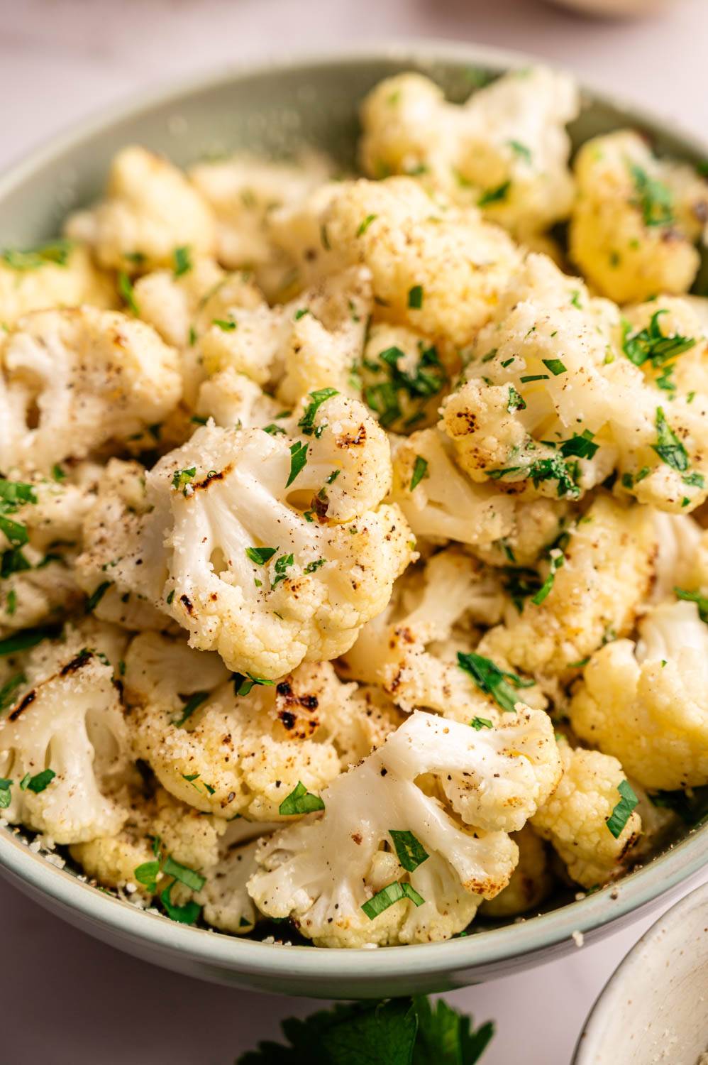 Close-up of roasted cauliflower florets in a bowl, lightly browned, garnished with chopped parsley. 
