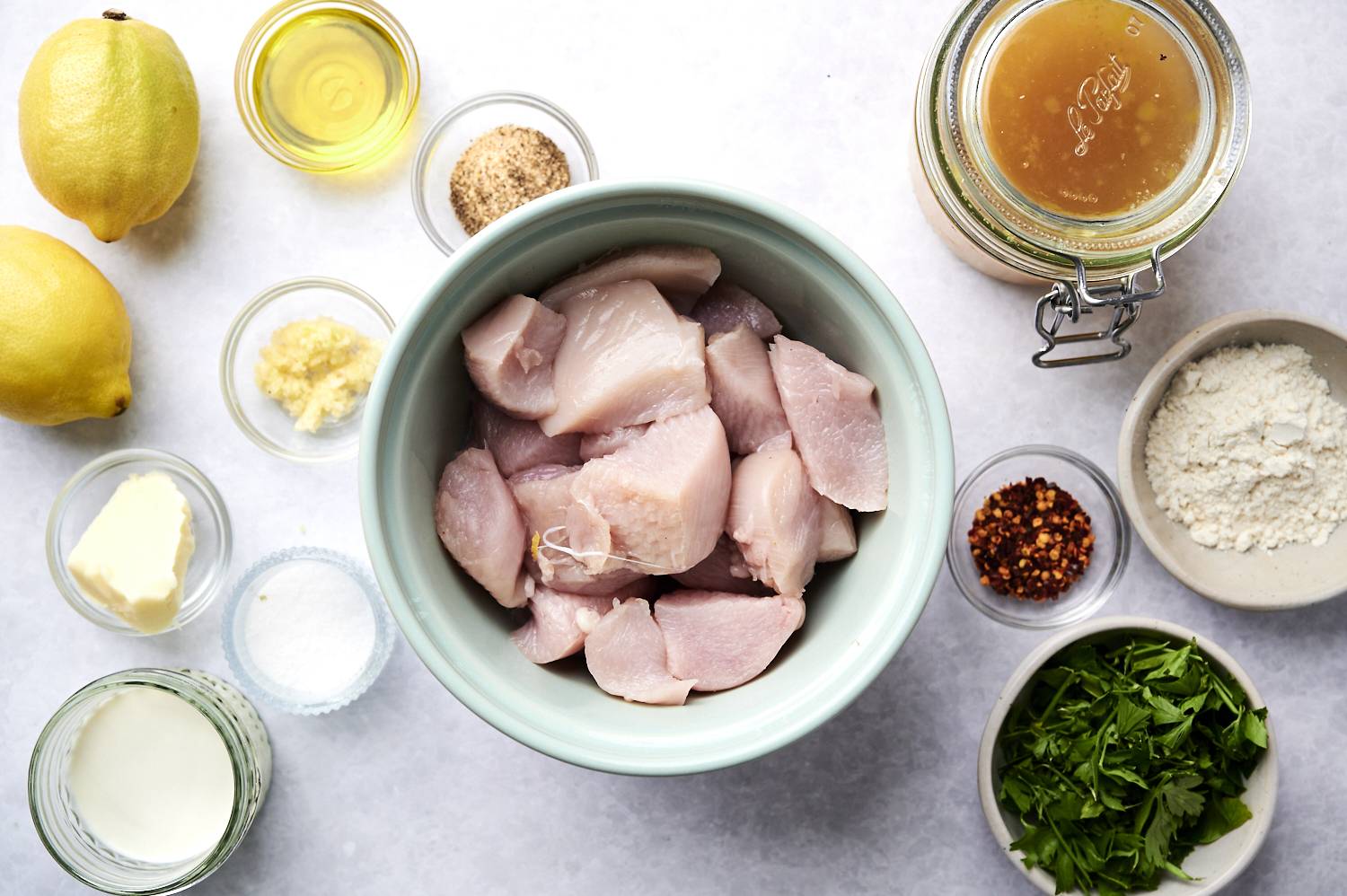 Ingredients for sauteed lemon pepper chicke including chopped chicken breast, flour, garlic, lemon pepper seasoning, lemons, chicken broth, parsley, and garlic.