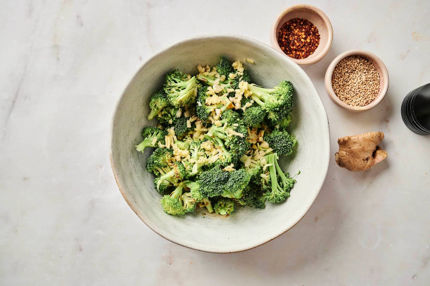 Ingredients for sesame broccoli including florets, garlic, and ginger in a bowl.