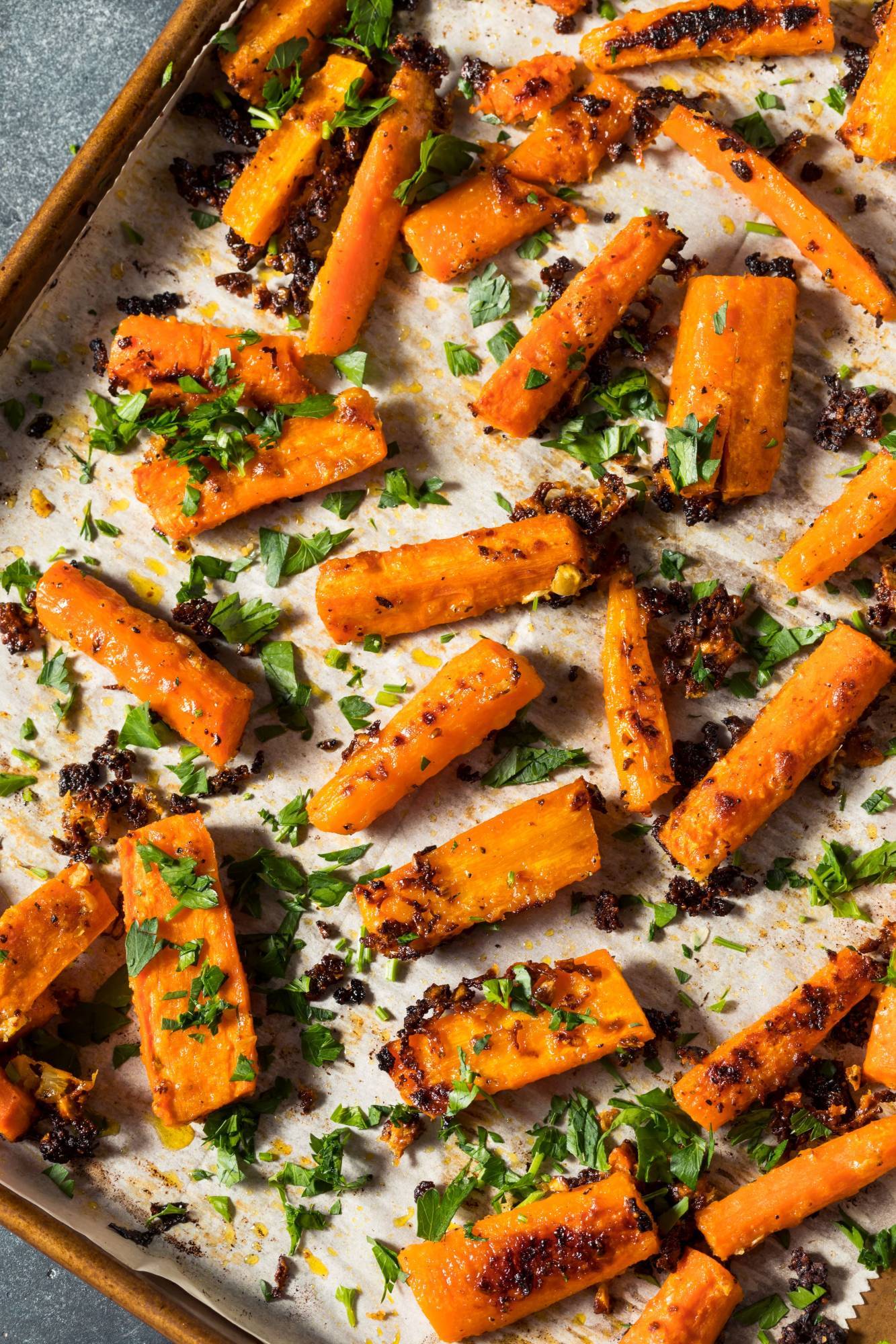 Asian roasted sesame carrots on a baking sheet with olive oil, cilantro, soy sauce, and pepper.