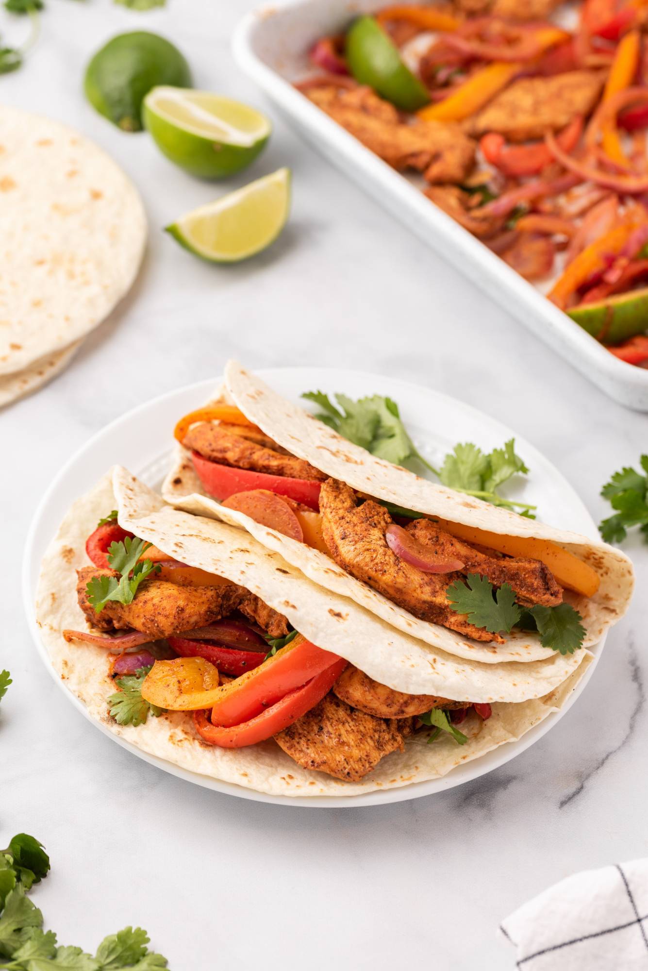 Chicken fajitas made on a sheet pan and served in flour tortillas with bell peppers, cilantro, lime, and red onion.