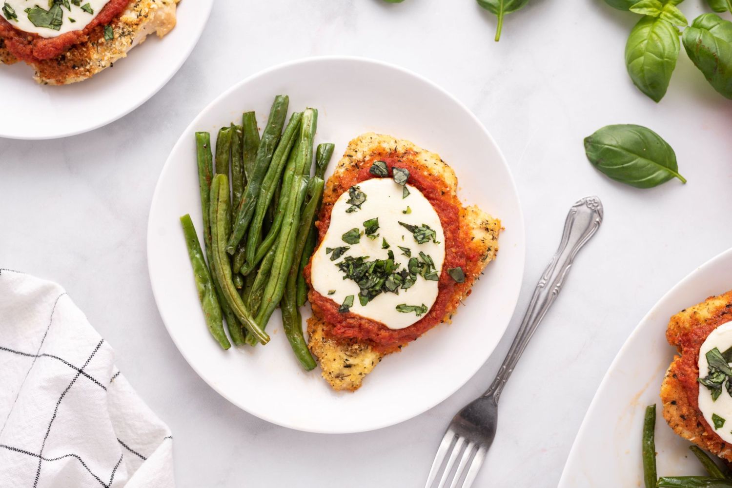 Healthy chicken parmesan with crispy baked chicken coated in marinara sauce and melted cheese on a plate with green beans.