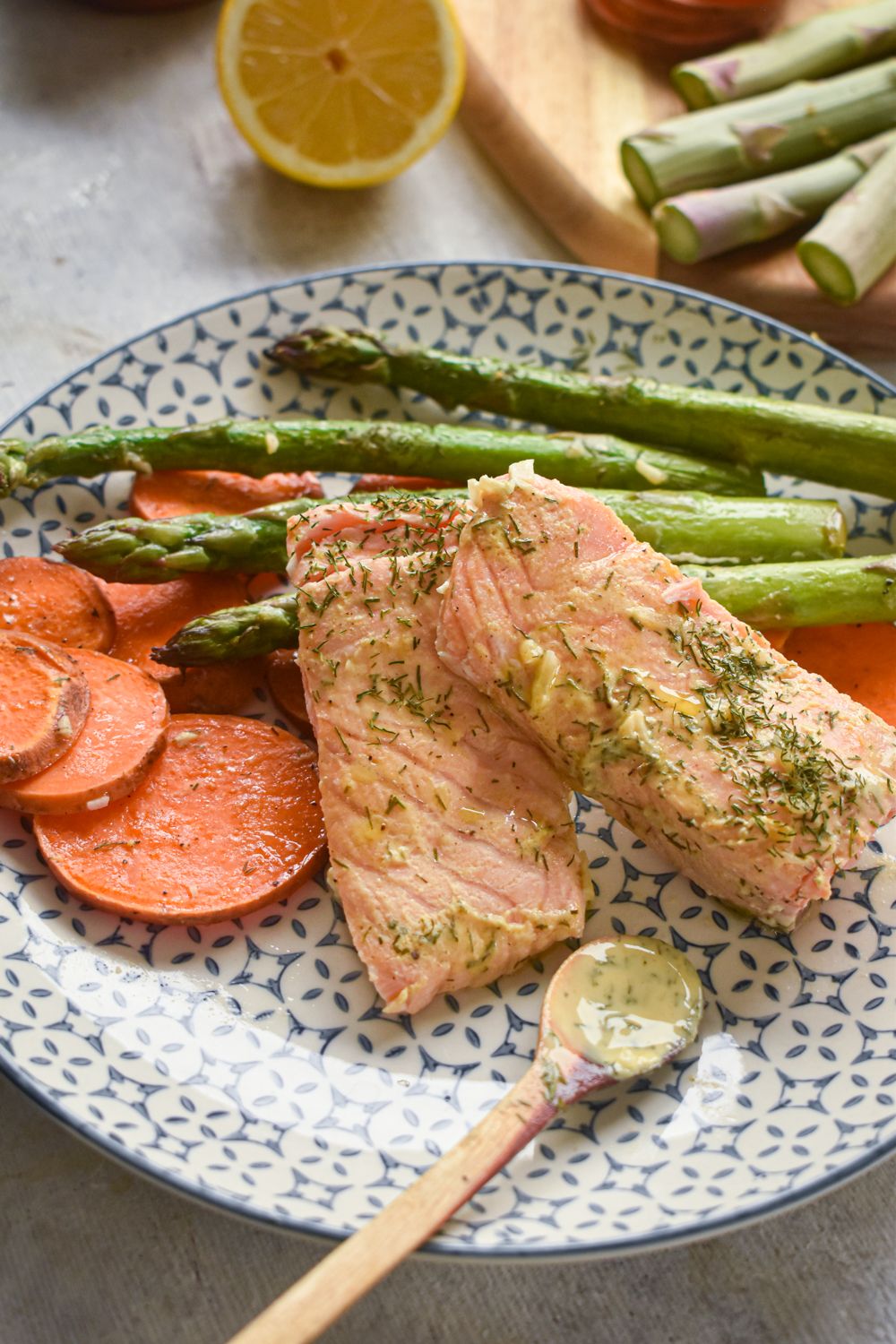 Roasted salmon with sweet potatoes, asparagus, and a lemon dill sauce on a plate.
