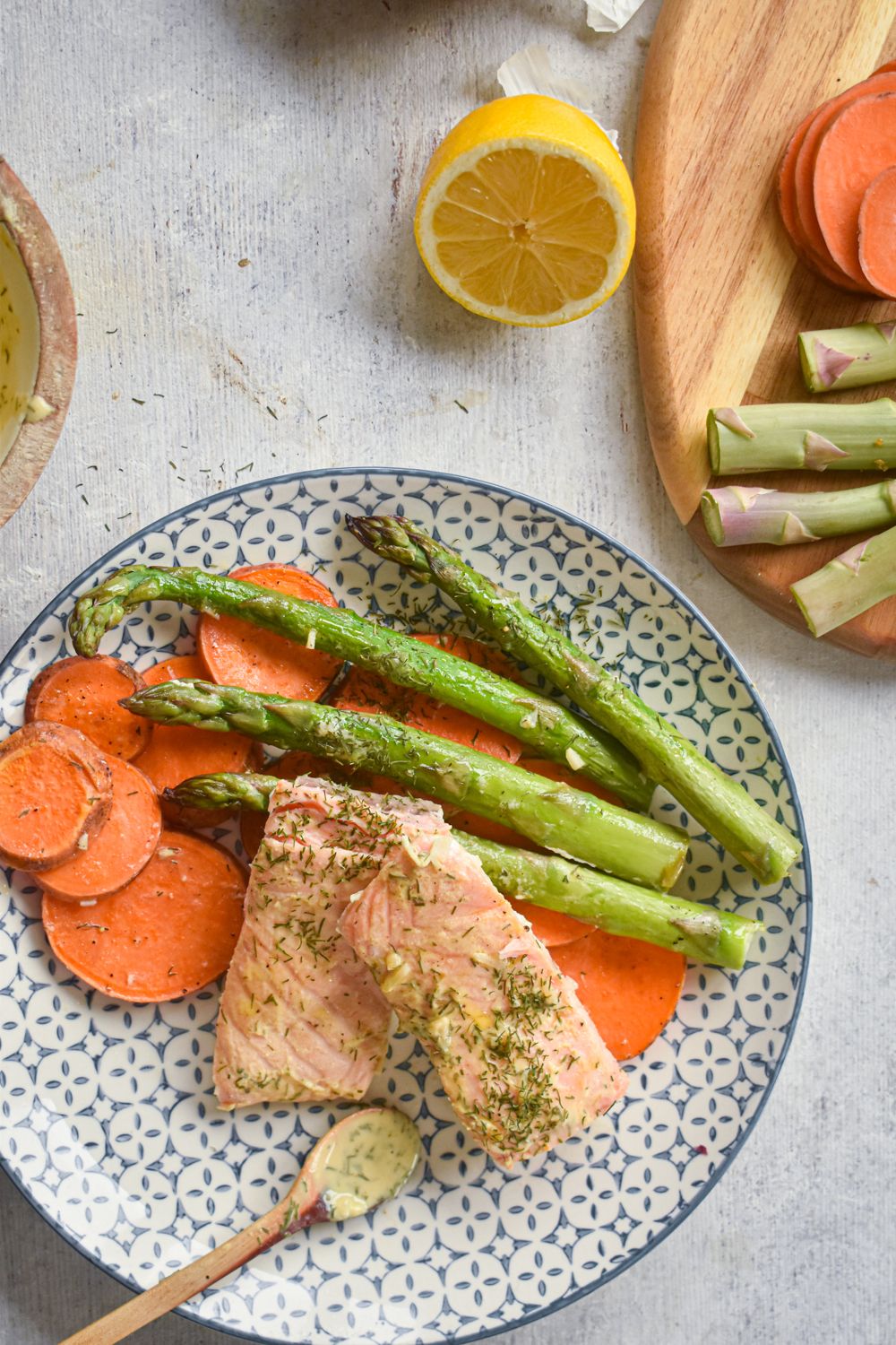 Sheet pan salmon with asparagus and sweet potatoes on a plate with lemon and dill sauce.