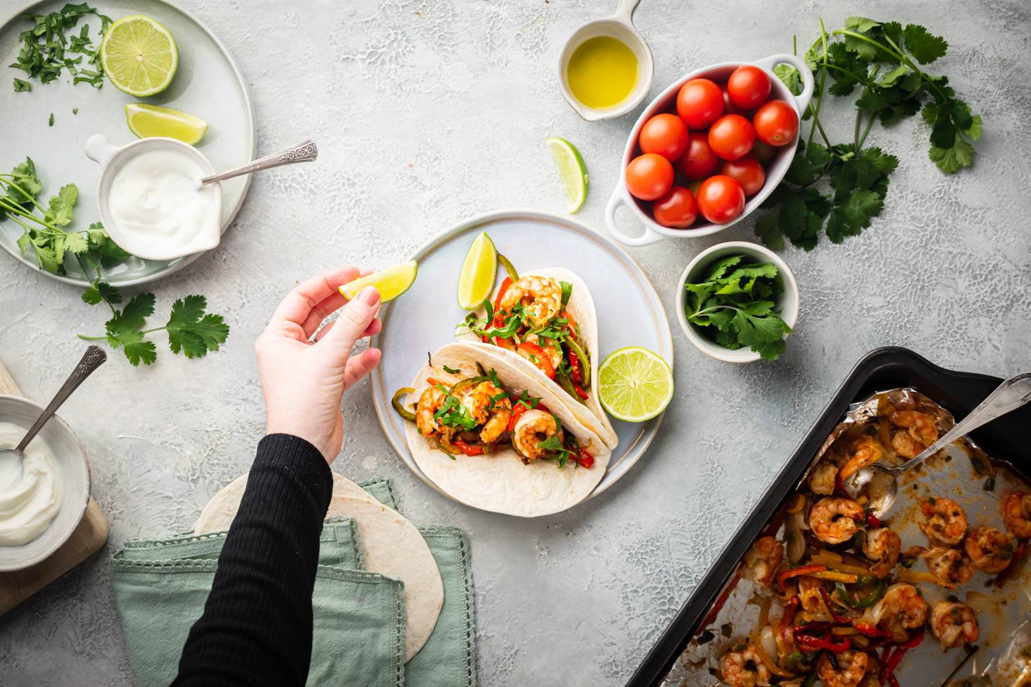 Shrimp fajitas made on a sheet pan served in warm corn tortillas with a lime being squeezed on top.
