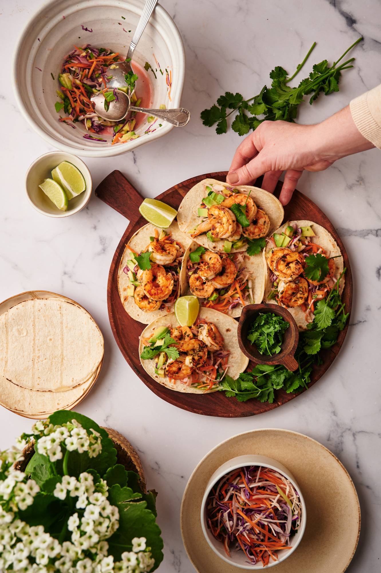 Easy shrimp tacos with shredded cabbage and avocado salsa served on corn tortillas with limes.