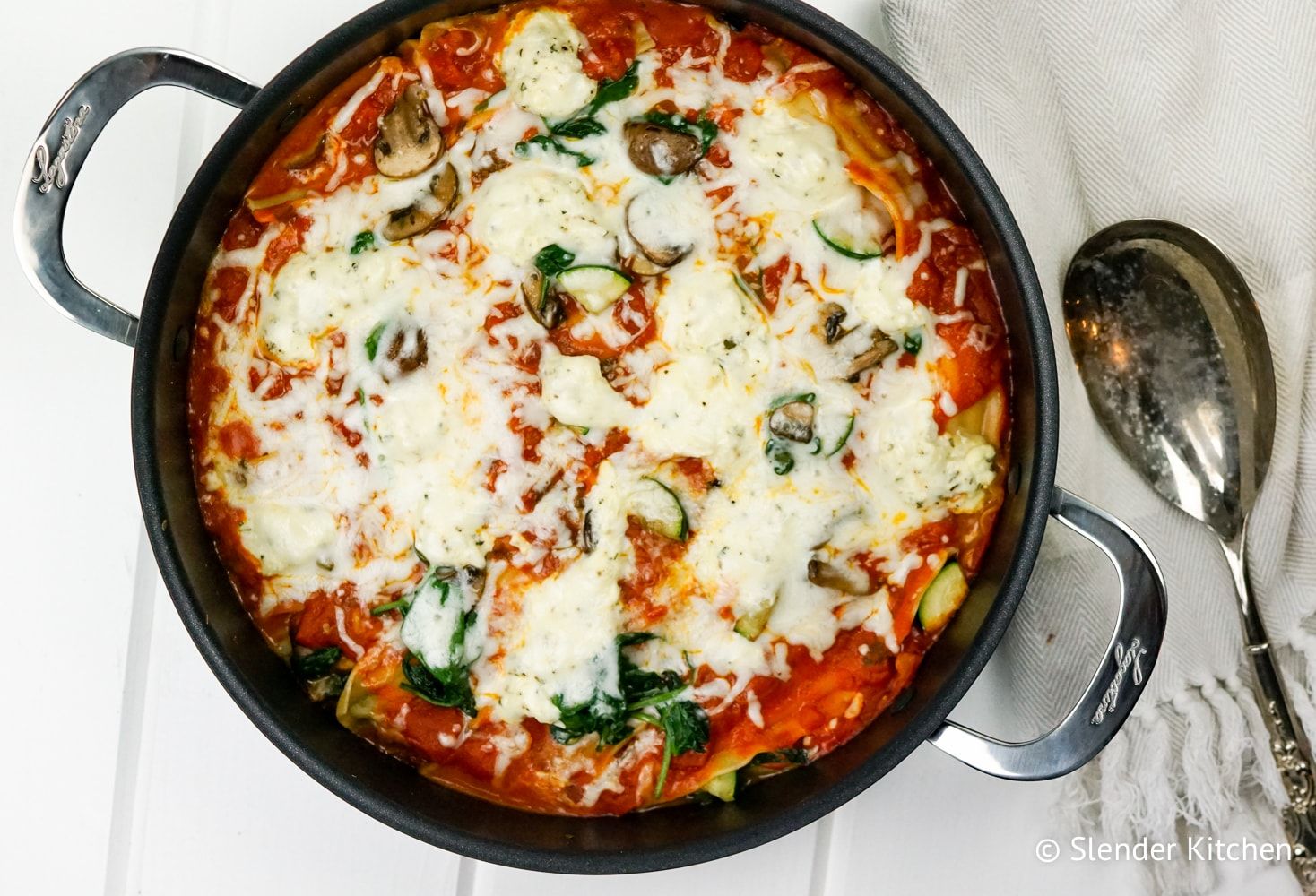 Skillet lasagna with mushrooms, spinach, lasagna noodles, sauce, and a layer of melted cheese in a skillet.