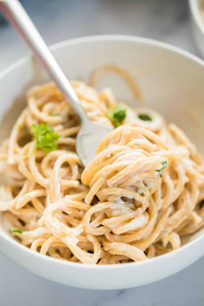 Creamy cauliflower Alfredo sauce served with spaghetti in a bowl being twirled with a fork.