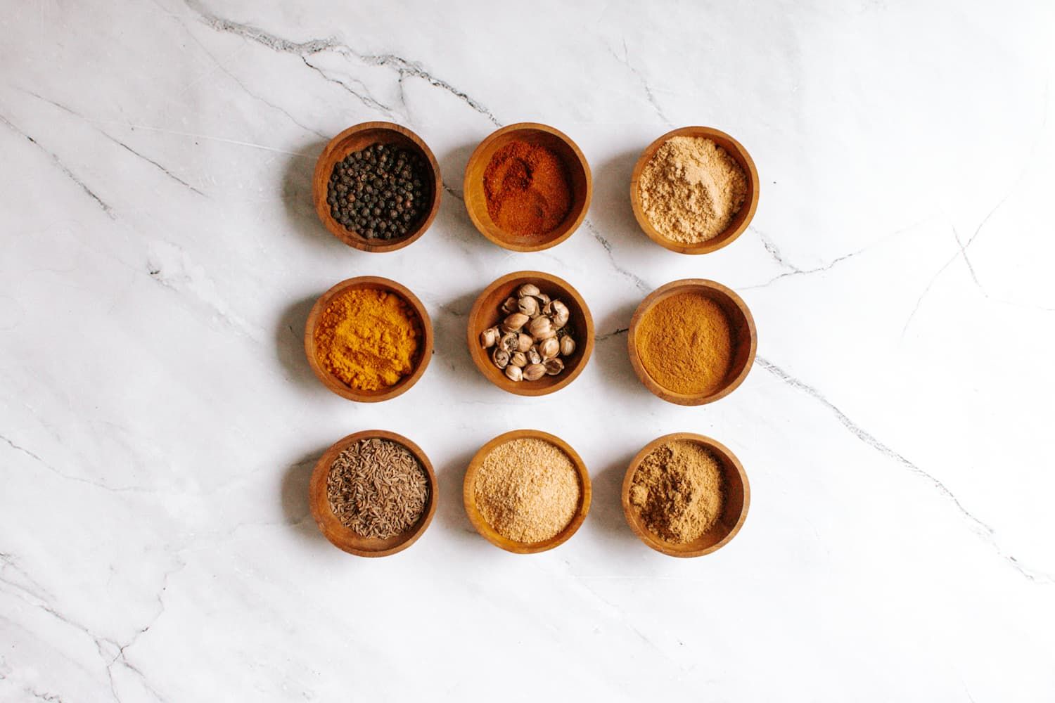 The spices needed  for curry powder in small wooden bowls including cumin, coriander, cardamom, and other spices.