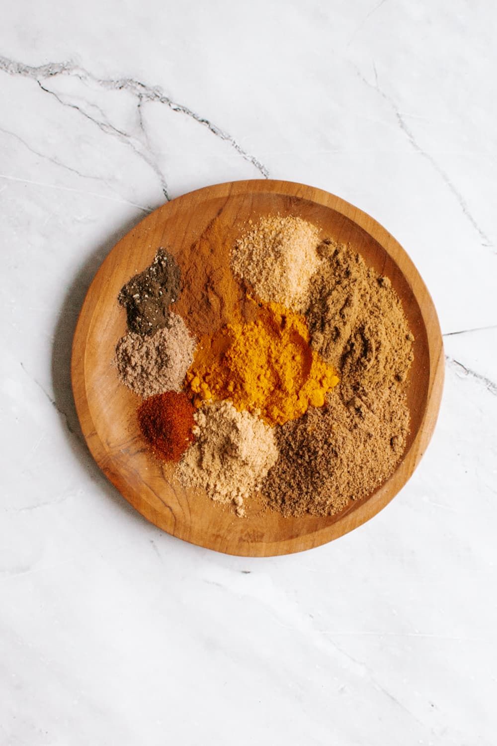 Curry spices including cumin, coriander, cinnamon, cardamom, and ginger on a plate  with a spoon.