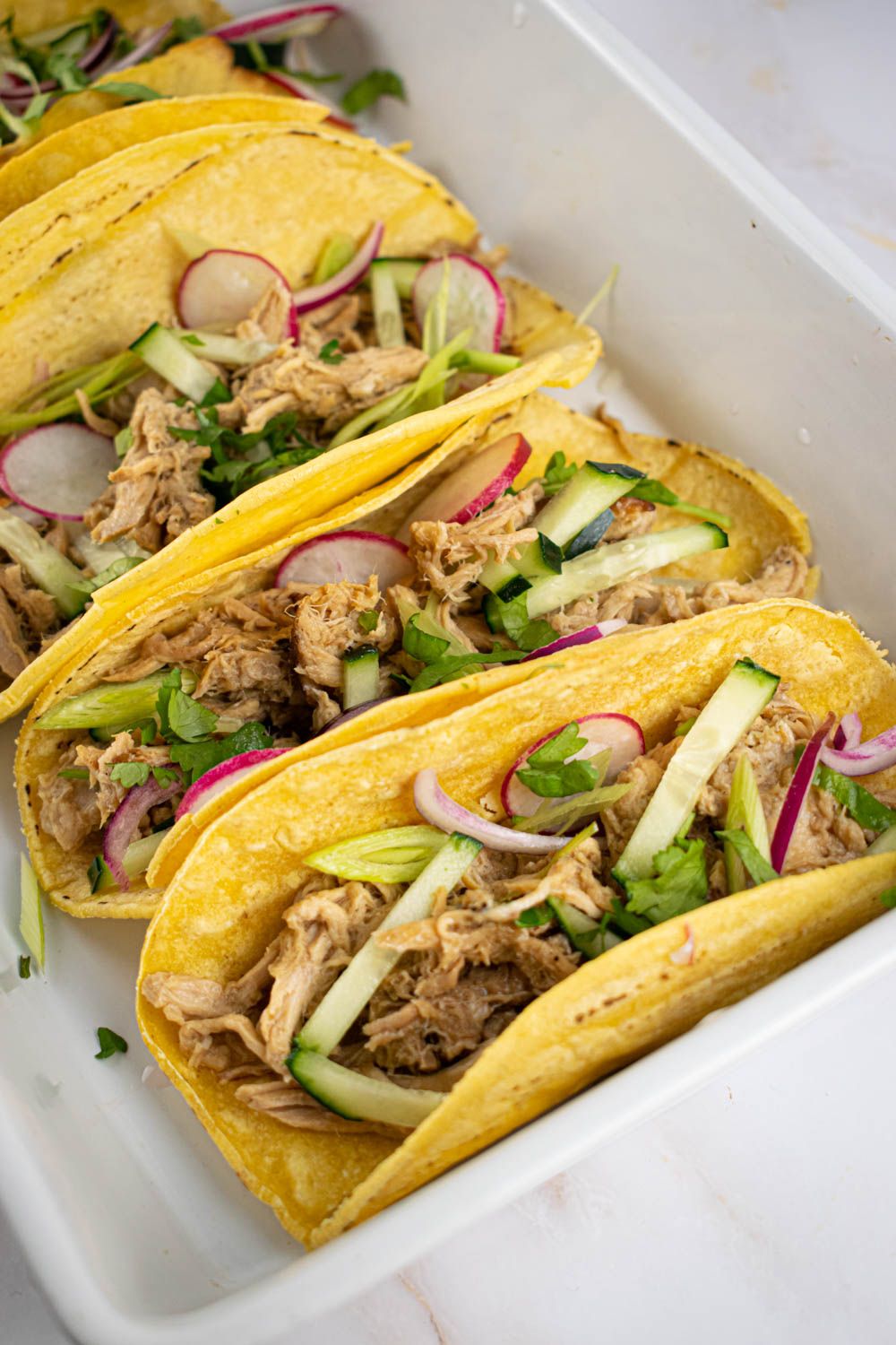 Crockpot pokr banh mi with radishes, cucumbers, and green onions in corn tortillas.