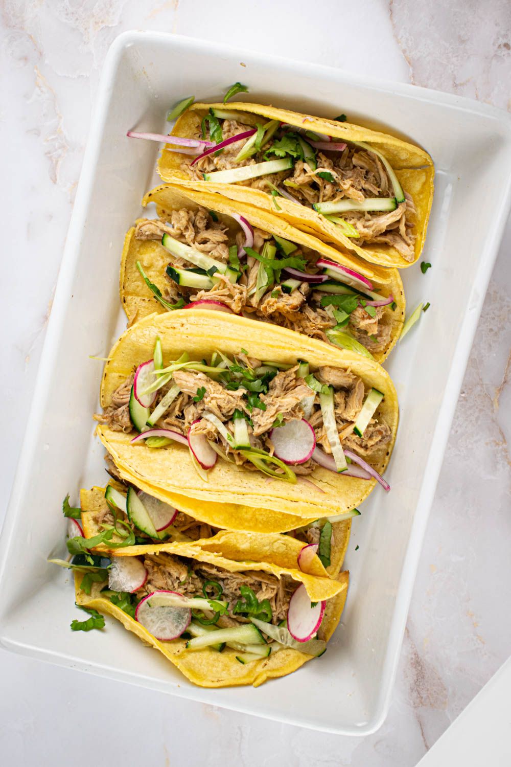 Banh Mi Pork in corn tortillas with sliced cucumbers, radishes, and green onions.