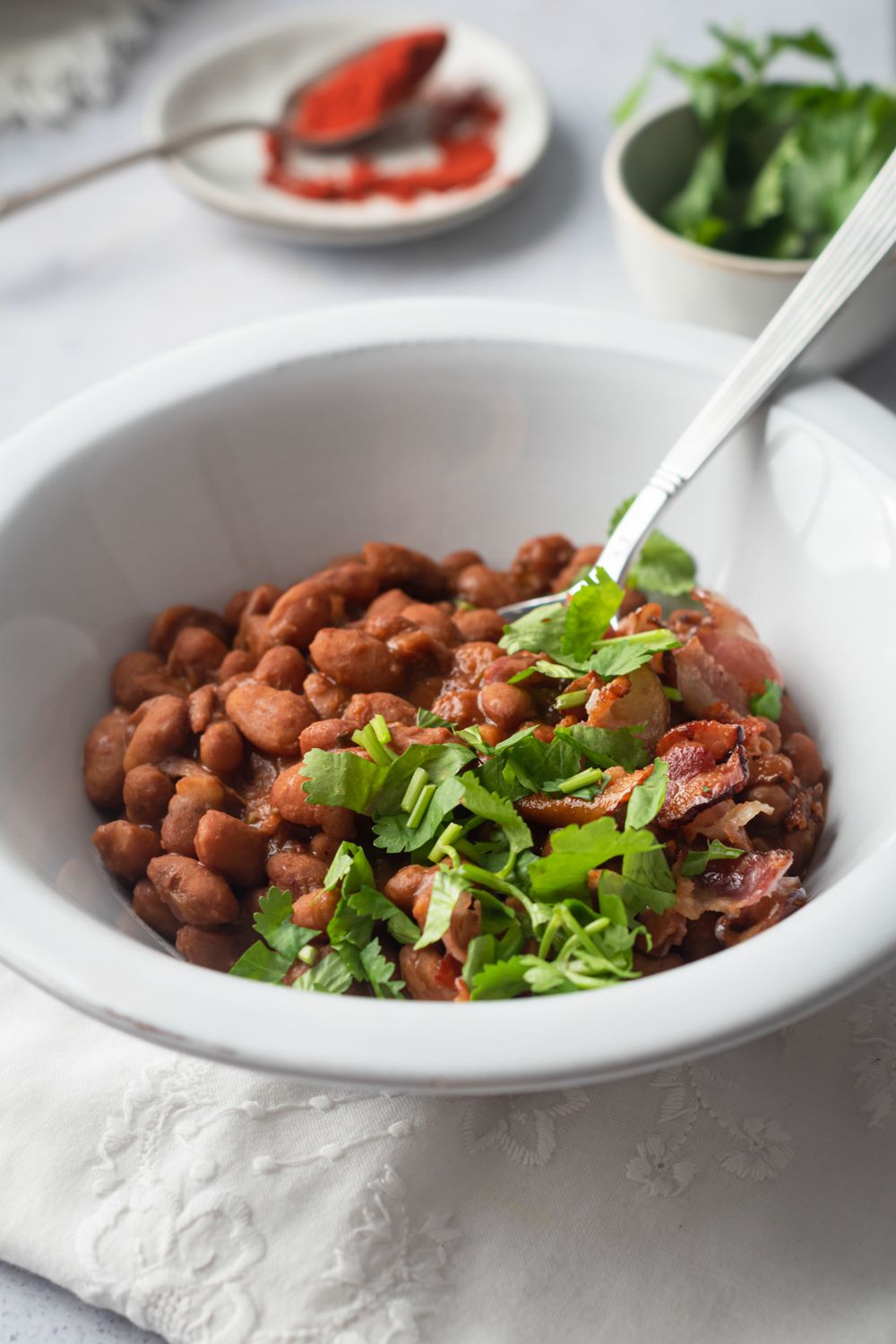 Borracho beans in a white bowl with cooked pinto beans, cilantro, bacon, jalapenos, and beer broth.