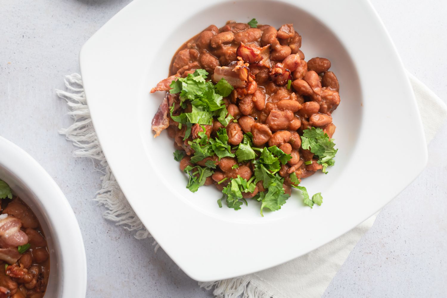 Crockpot borracho beans served in a white bowl with crispy bacon pieces and fresh cilamtro.