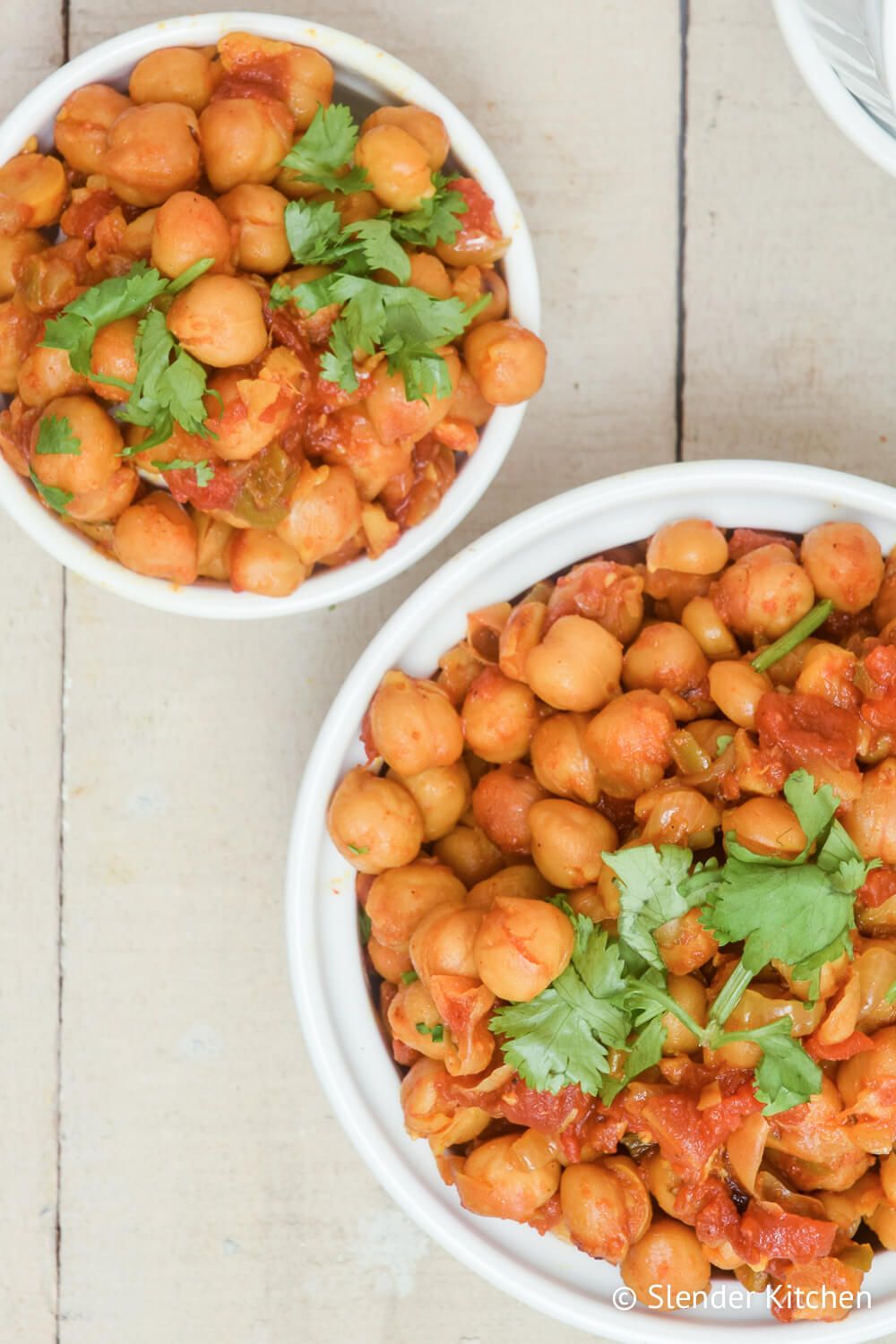 Chana masala with chickpeas cooked in curry tomato sauce in two white bowls.