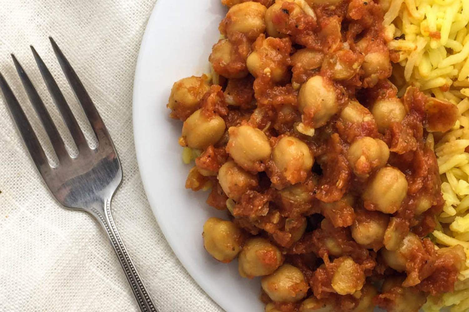 Crockpot chana masala with rice on a white plate with a fork