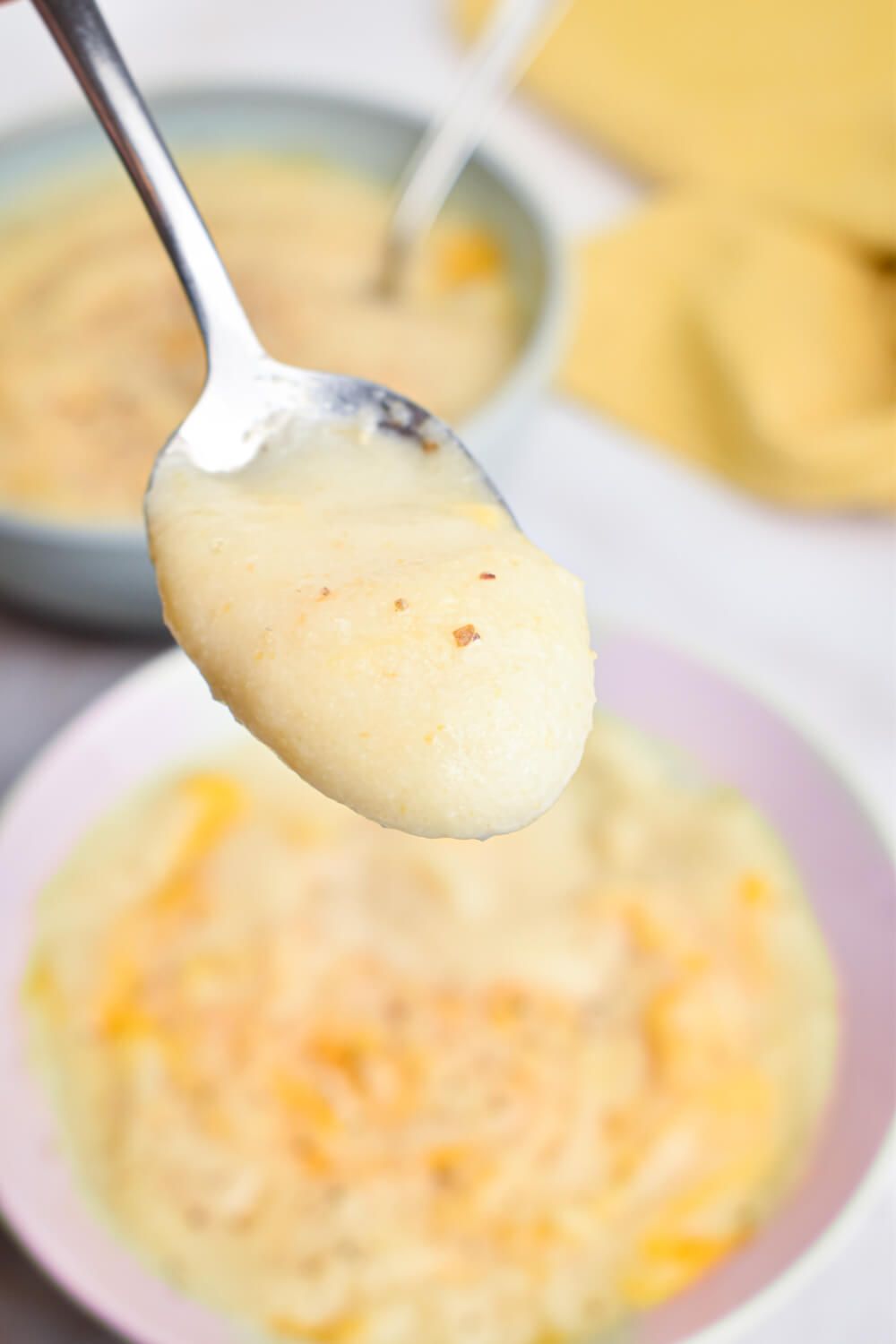 Cauliflower soup in a bowl with a spoon, cheddar cheese, and fresh black pepper.