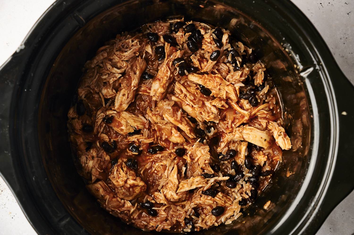 Slow cooker with shredded chicken, black beans, salsa, and rice for burrito bowls.