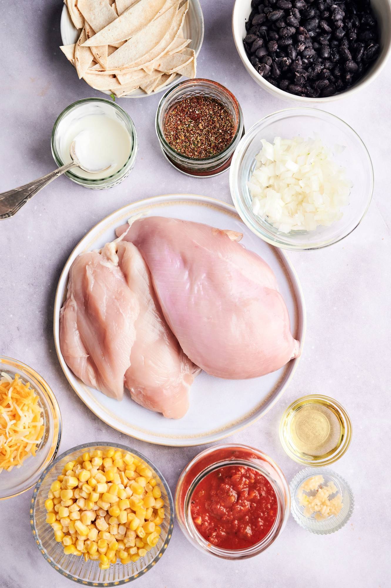 Ingredients for crockpot chicken enchilada casserole including chicken breast, corn tortillas, cheese, black beans, corn, enchilada sauce, and sour cream.