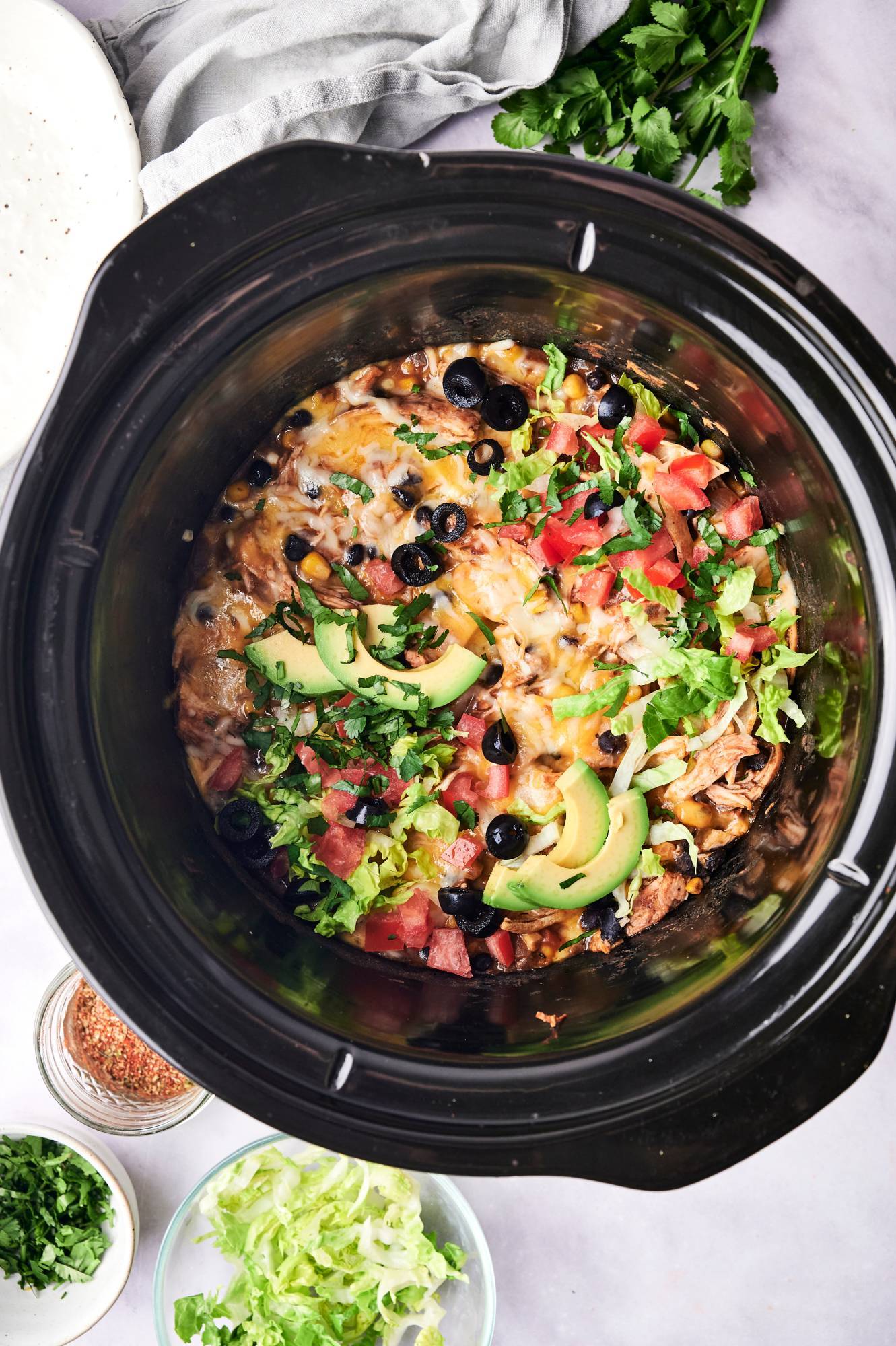 Crockpot chicken enchilada casserole with shredded chicken, corn tortillas, avocado, black olives, black beans, corn, and melted cheese.