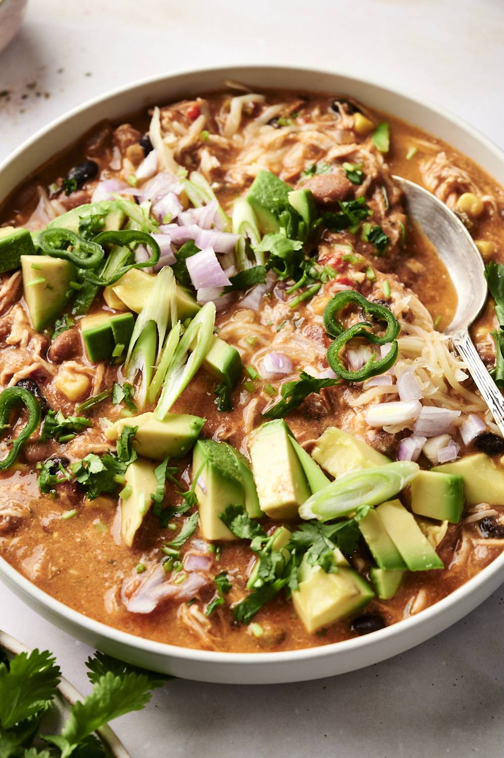 Crockpot enchilada soup with cheese, jalapenos, avocado, cilantro, and green onion in a bowl.