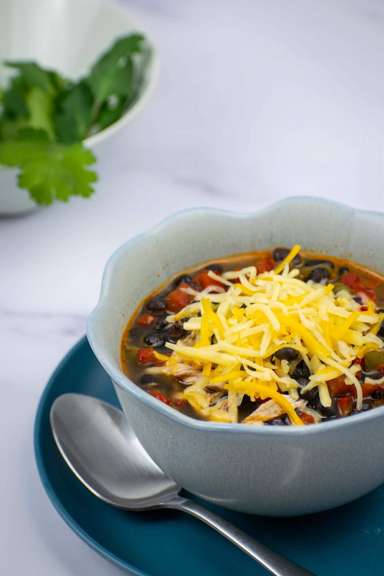 Crockpot Chicken Enchilada Soup in a blue bowl with shredded cheese.