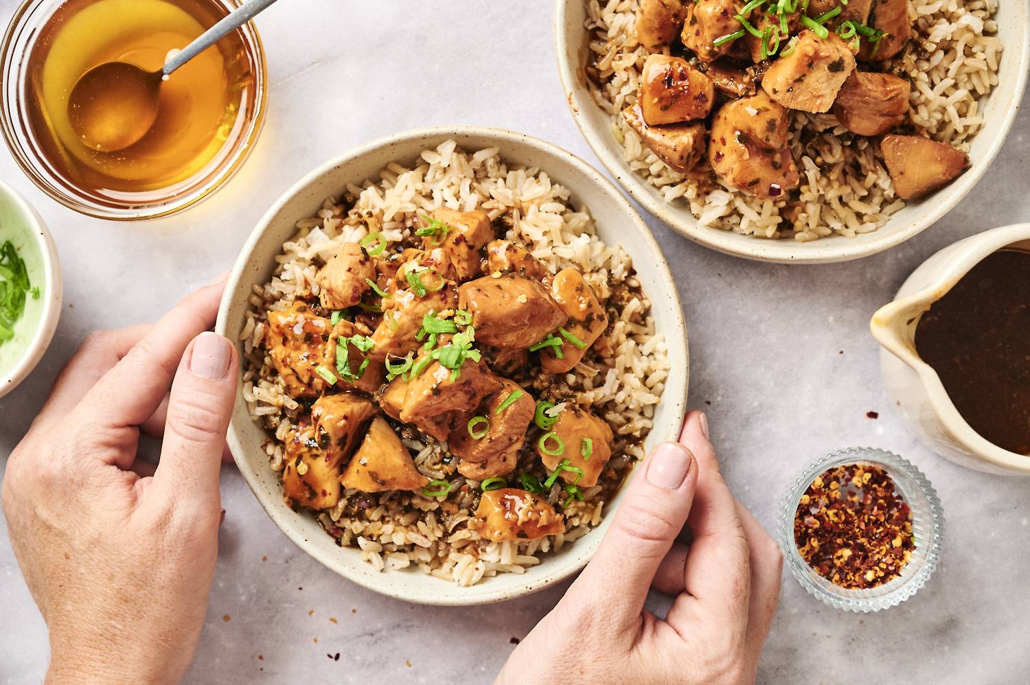 Honey garlic chicken in two bowls with rice and green onions.