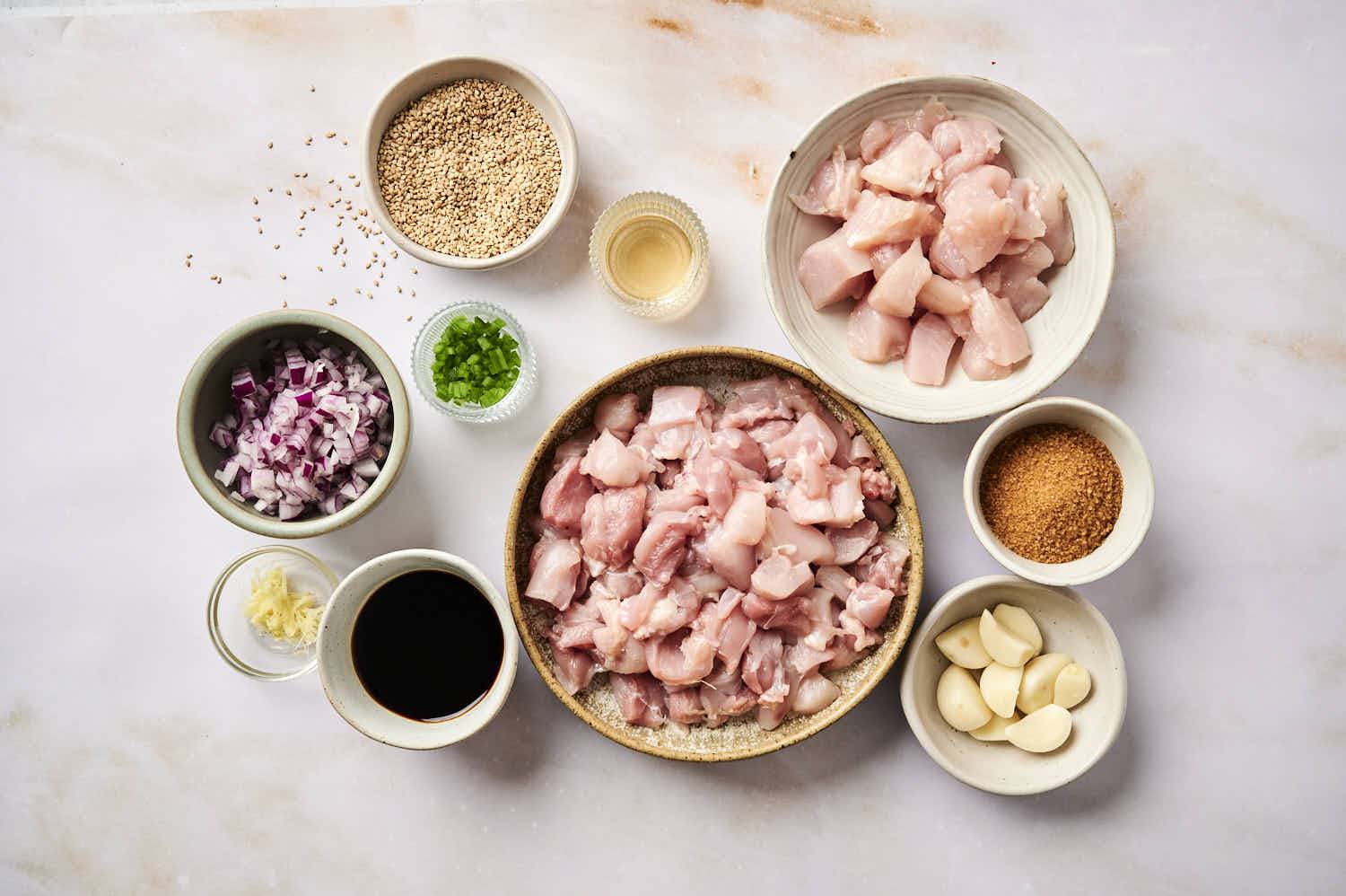 Ingredients for slow cooker Korean chicken including chicken, garlic, brown sugar, onions, soy sauce, ginger, and sesame seeds.