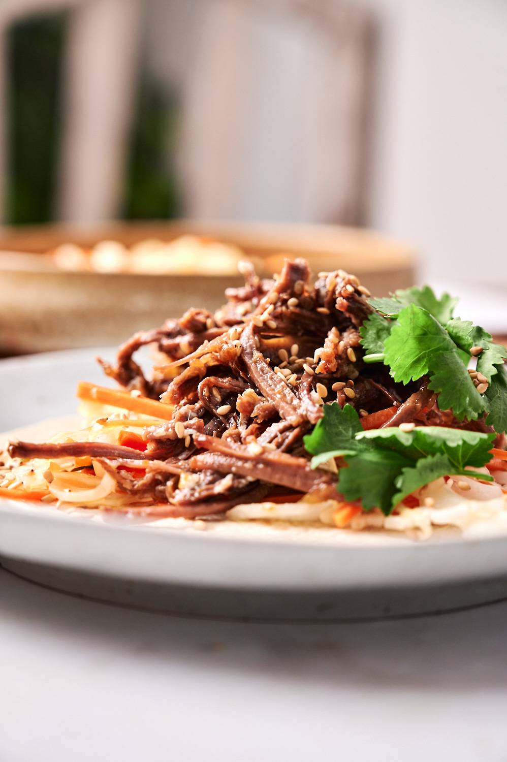 Korean tacos with shredded beef, coleslaw, hot sauce, and sesame seeds on a corn tortilla.