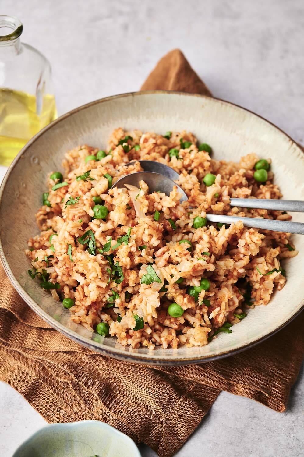 Bowl of fluffy slow cooker Mexican rice with green peas and fresh cilantro, served with a silver spoon on a brown napkin. 